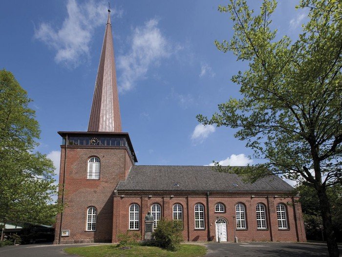 Kirche vor leicht bewölktem Himmel mit Bäumen.