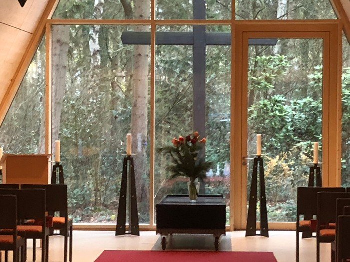 Blick aus der Waldfriedhofskapelle auf den Wald und das große Holzkreuz.